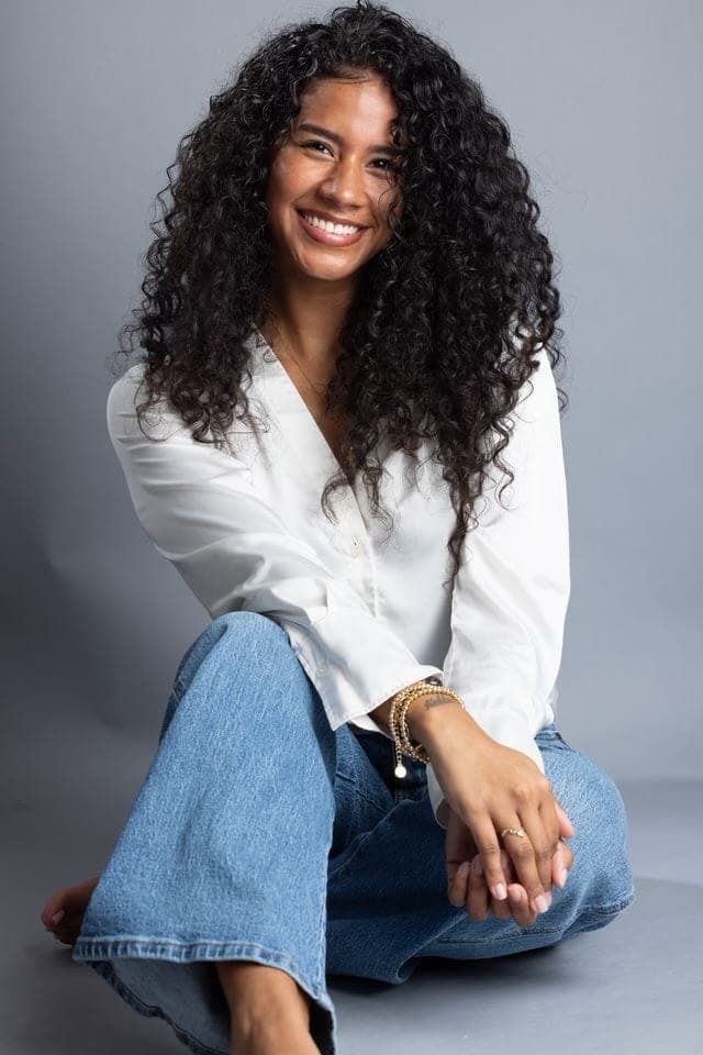 Nicol Rios smiling, seated in a white blouse and jeans.